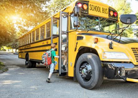 A student boarding a school bus during the morning with golden sunlight in the background.